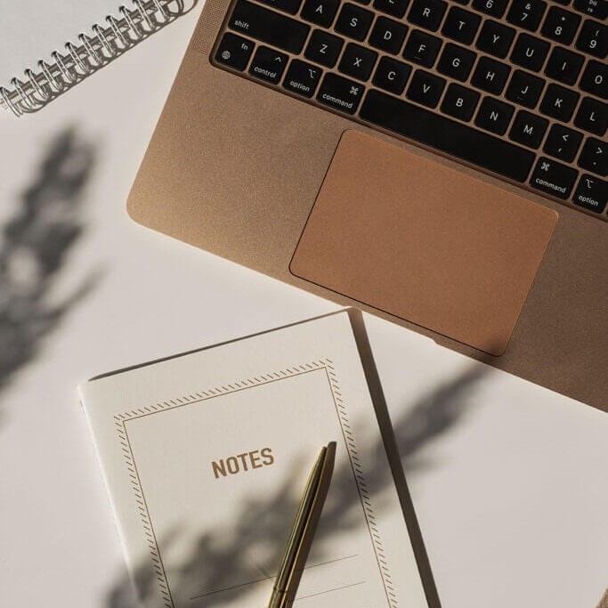 Overhead view of a laptop, notebook labeled NOTES, and a pen, representing adult counseling sessions and reflection.